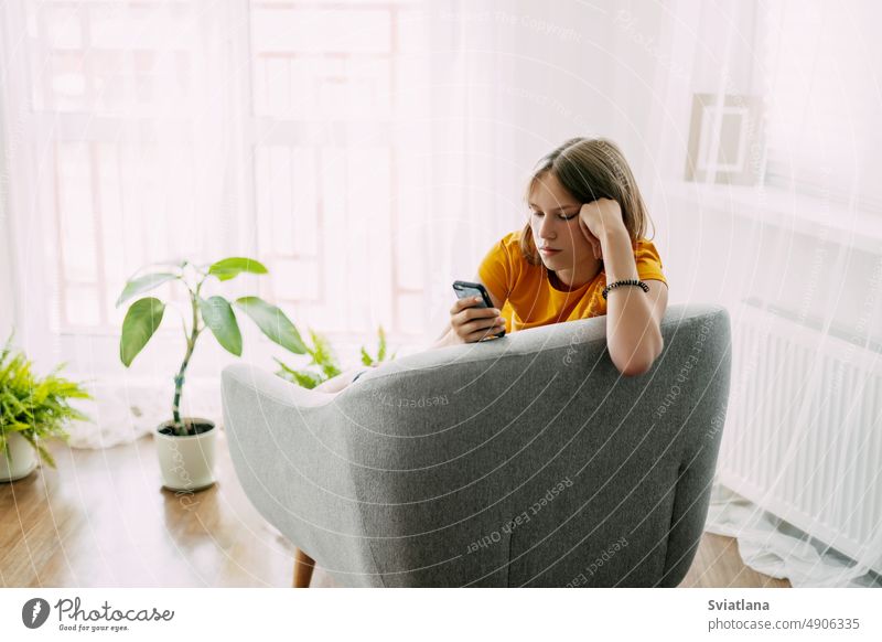 A young girl is sitting in a chair and exchanging messages online on her phone. Home recreation, modern lifestyle student messaging using communication message
