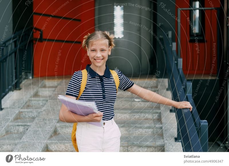 A smiling teenage girl with a backpack and a folder in her hands goes down the stairs, hurries to school. Back to school, high school student steps teenager