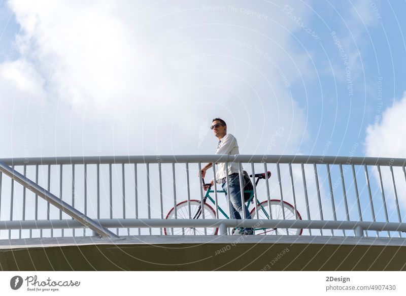 young hipster man riding fixed gear bike on city bridge sunglasses standing sky bicycle person outdoor travel urban lifestyle ride bicyclist biking road cycling