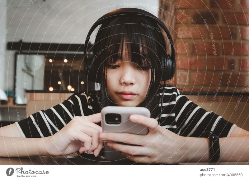Teenage girl wearing headphones and holding a cell phone smartphone social media relaxing on the sofa. earphones mobile phone music listening person woman