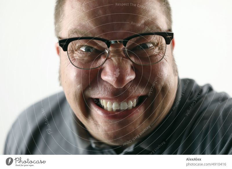 Very close portrait of a man grinning and looking madly at the camera - and wearing black-rimmed vintage glasses Man Wild Madness fun Joy Intensive very close