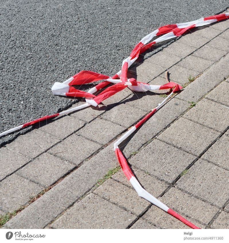 torn red and white barrier tape lies on the ground on paving stones and asphalt flutterband cordon corrupted Broken torn down Paving stone Asphalt Protection