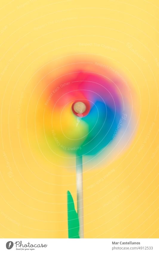 Moving coloured pinwheel on yellow background. Vertical photo. Thematic lgtbq. plastic summer toy wind windmill fun blue color happy rainbow energy joy colorful