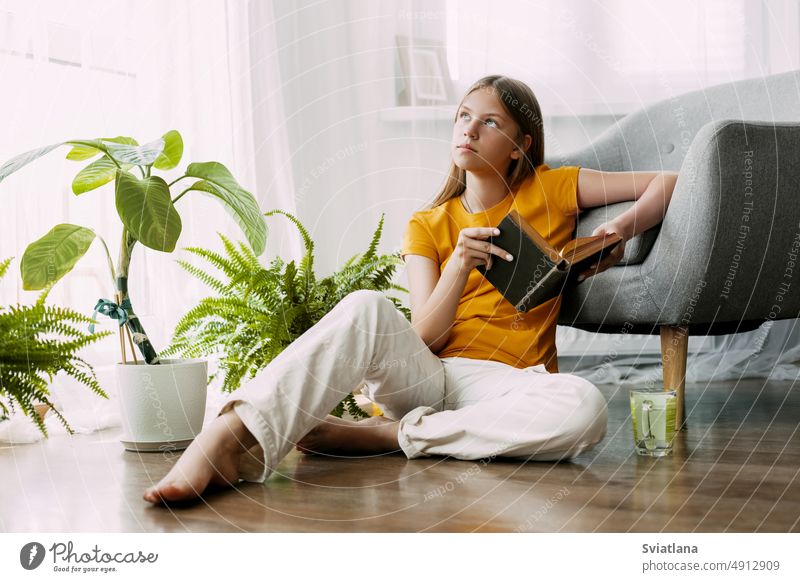 An attractive girl is reading a book, sitting on the floor of the house, having a good time. Rest, relaxation student study educational back to school knowledge