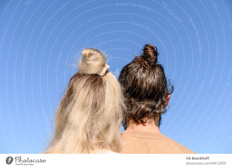 A couple with blonde and black hair and each with chignon from behind Chignon Sky man and woman Couple Colour photo Exterior shot Day Looking away Rear view