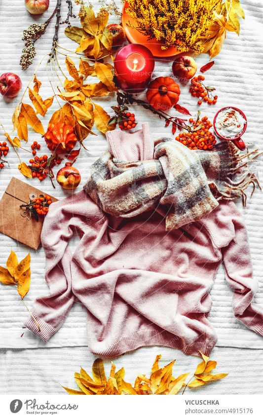 Autumn lifestyle with knitted sweater, orange leaves, candles, pumpkins and hot chocolate at white fabric background. Cozy seasonal fashion concept with pullovers and decoration