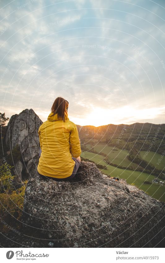 Sunrise at Sulov rocks in eastern Slovakia. Beautiful brunette sits on the rock in yellow jacket. Rough untouched landscape with rocks in orange light.