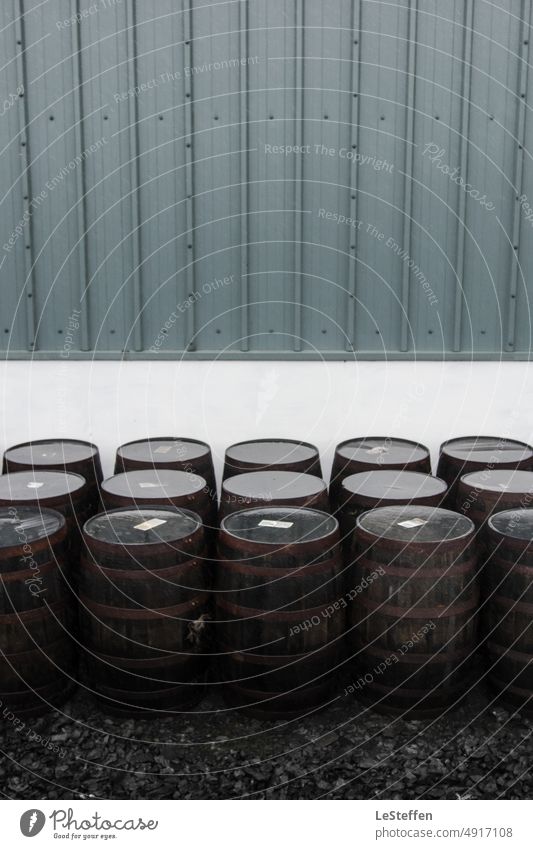 Whisky barrels stand outside a Scottish distillery after the rain. Barrels Keg Scotland Water reflection Minimalistic Modern Cold symmetry Dark white wall Metal