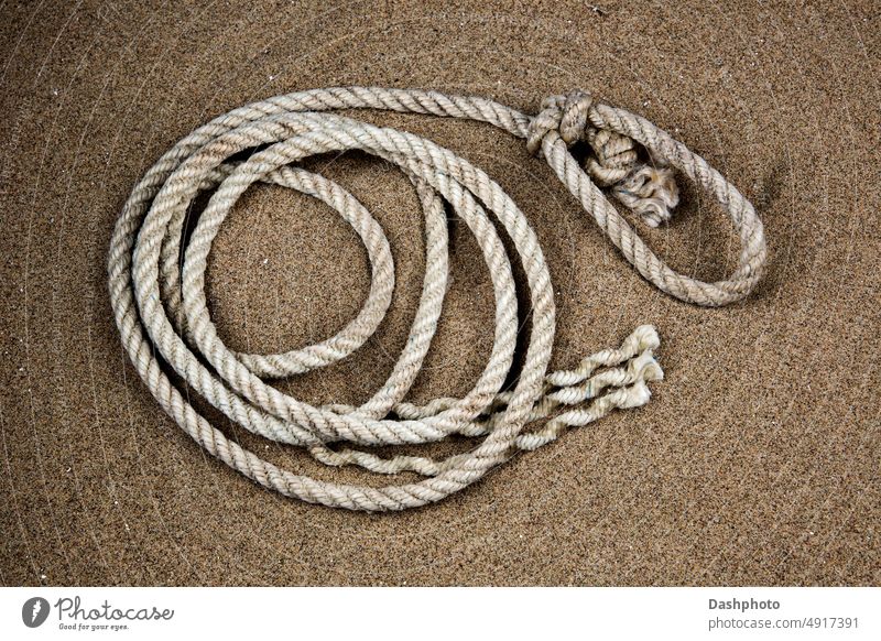 Coil of Old Rope on a Sandy Coastal Beach rope old coil old rope coiled rope white grey gray sand sandy brown knot noose loop strands beach coast coastal