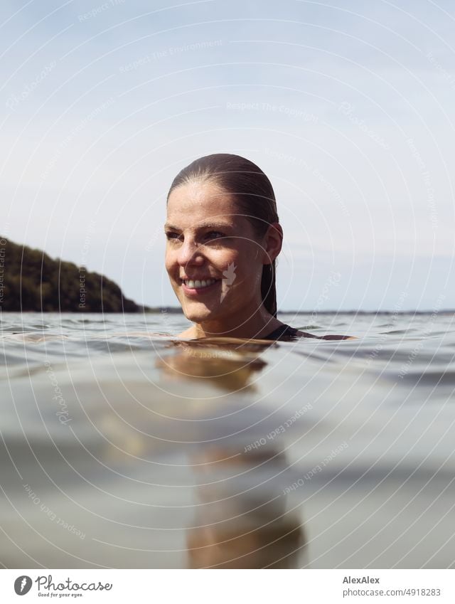 Young beautiful woman in the shallow water in the Baltic Sea looks to the side and smiles Lifestyle Back-light salubriously pretty Woman Athletic Slim Esthetic