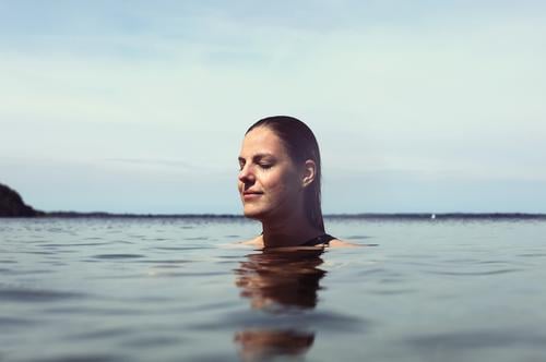 Young beautiful woman in the shallow water in the Baltic Sea smiles contentedly with closed eyes Lifestyle Back-light salubriously pretty Woman Athletic Slim
