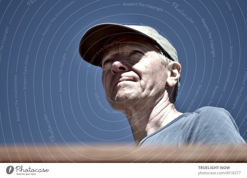 Way and goal concentrated in view: Man with baseball cap in front of  cloudless blue sky, sunlight and shadow on face, blue-grey t-shirt,  portrait, shot under eye - a Royalty Free Stock