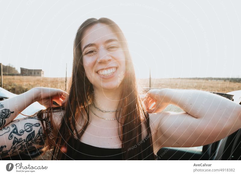 Portrait of a super happy smiling young woman with tattoos touching his hair during a sunset. Carefree holiday free time concept. Freedom and liberty concept. Gen Z outdoors fun. New life new days.