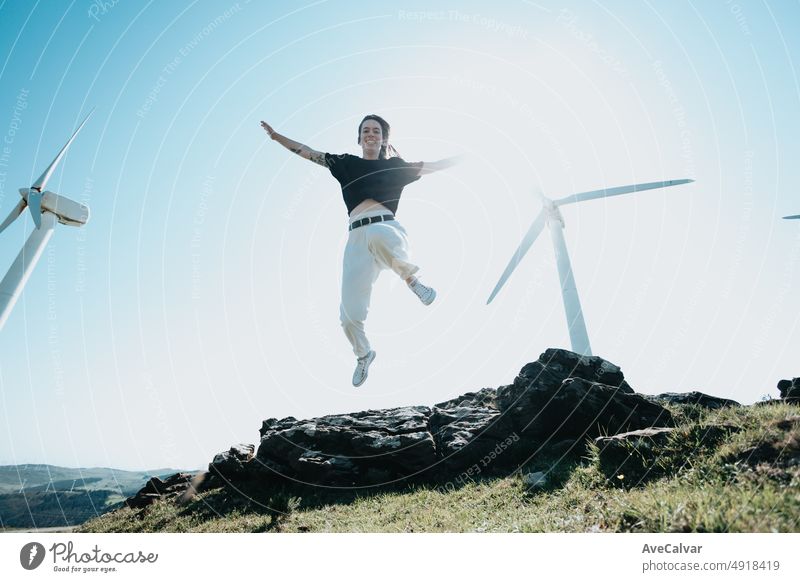 Young woman jumping in liberty surrounded by electric powered windmills. New sources of energy concept. Young conscious people, recycle, reuse, save the planet concept. Sustainable world