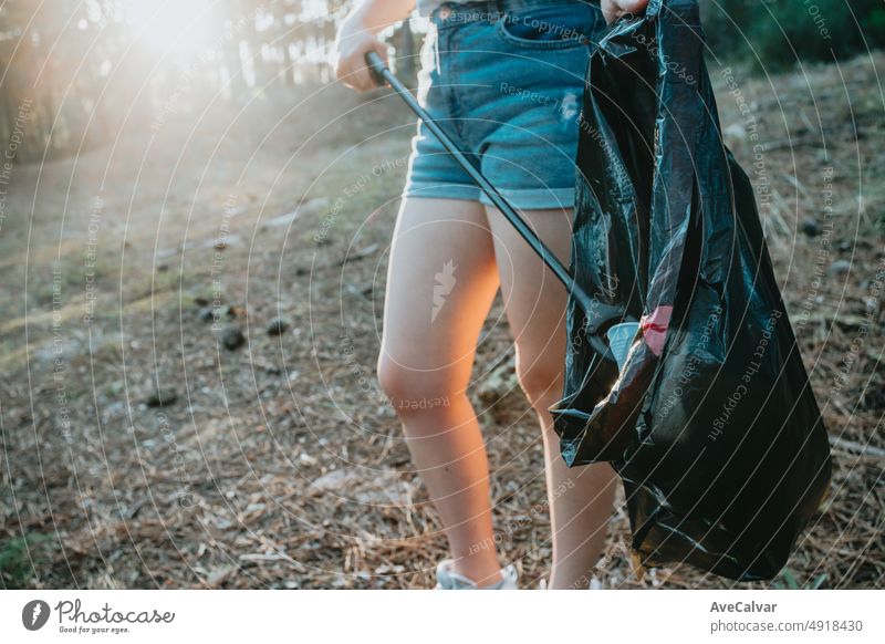 Young woman volunteer cleaning up the forest and collecting trash into a bag. Sustainability, save the planet .Nature cleaning, ecology green concept.Environment plastic pollution with copy space