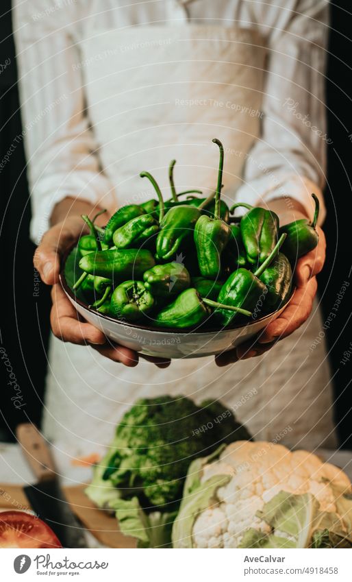 Close up image of an old woman cooking chef grabbing peppers of padron and showing to camera before preparing them in a healthy food.Rustic cuisine cooking made by chef.