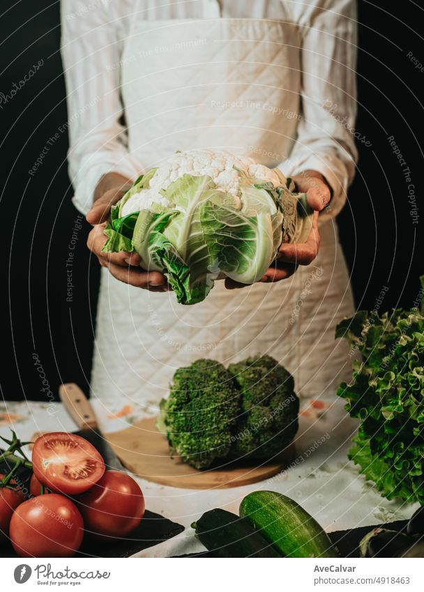 Close up image of an old woman cooking chef grabbing cauliflower and showing to camera before preparing them in a healthy food.Rustic cuisine cooking made by chef. Preparing ingredient for a bio meal.