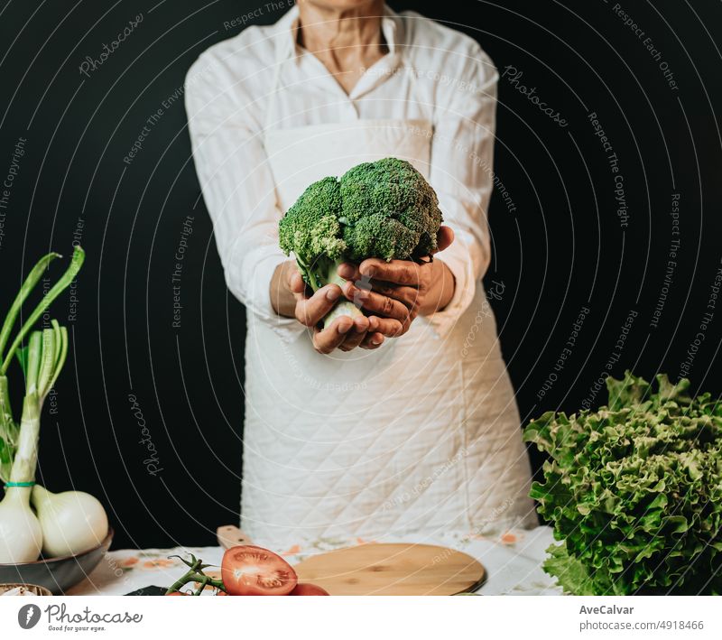 Close up image of an old woman cooking chef grabbing broccoli and showing to camera before preparing them in a healthy food.Rustic cuisine cooking made by chef. Preparing ingredient for a bio meal.