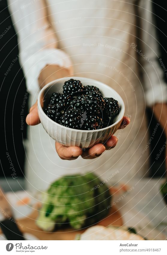Close up image of an old woman cooking chef grabbing blackberry offering to camera before preparing them in a healthy food.Rustic cuisine cooking made by chef. Preparing ingredient for a bio meal.