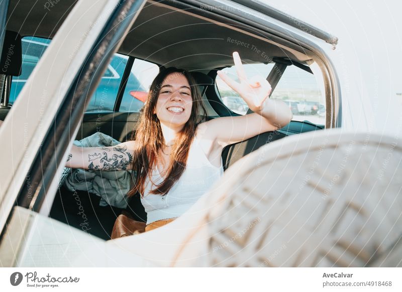 Super happy and positive smiling young woman with tattoos resting back in her car after a road trip day. Carefree holiday free time concept. Freedom and liberty concept. Gen Z outdoors fun.