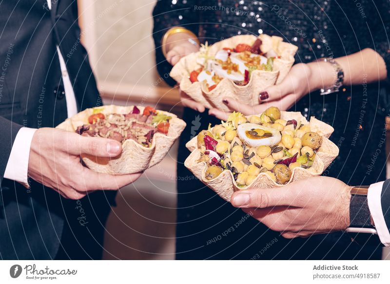 Anonymous friends with salads standing near wall group dinner meal dish tortilla bowl food restaurant bonding spare time elegant men woman occasion suit