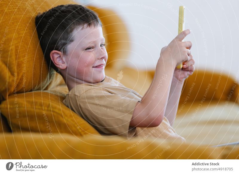 Happy boy sitting on a sofa browsing on smartphone child home happy smile delight technology kid young concentrated cartoon movie lifestyle childhood glad