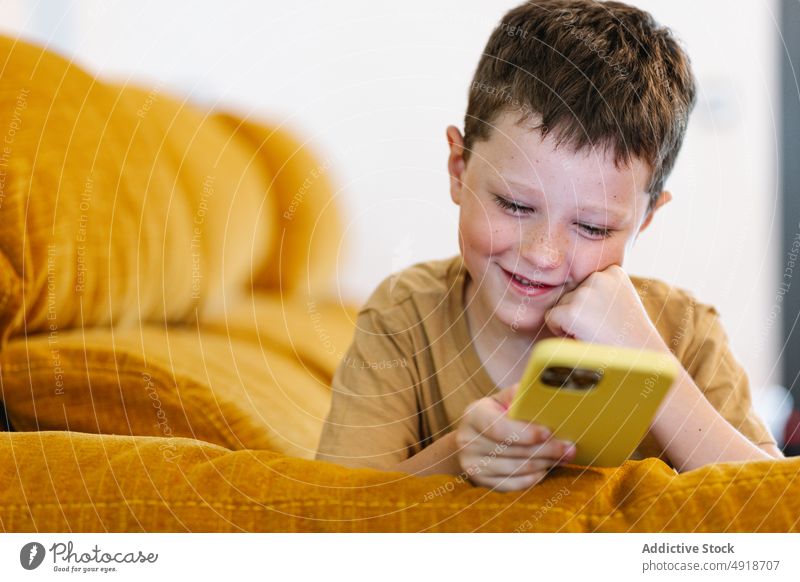 Happy boy lying on a sofa browsing on smartphone child home happy smile delight technology indoors kid young concentrated cartoon movie lifestyle childhood glad