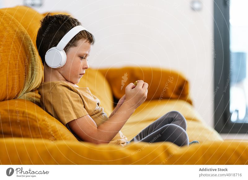 Boy sitting on a sofa using the mobile phone child boy home technology smartphone kid headphones young listen serious concentrated movie lifestyle