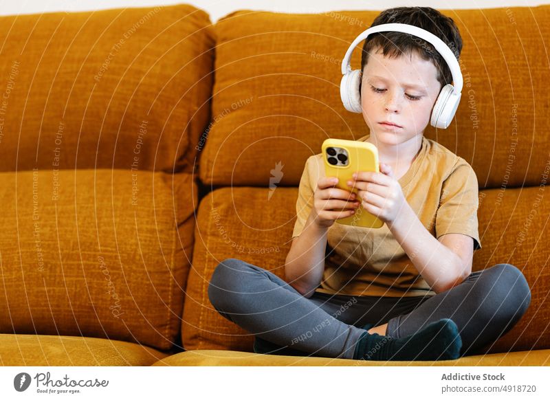 Boy sitting on a sofa using the mobile phone child boy home technology smartphone kid headphones young listen serious concentrated movie lifestyle