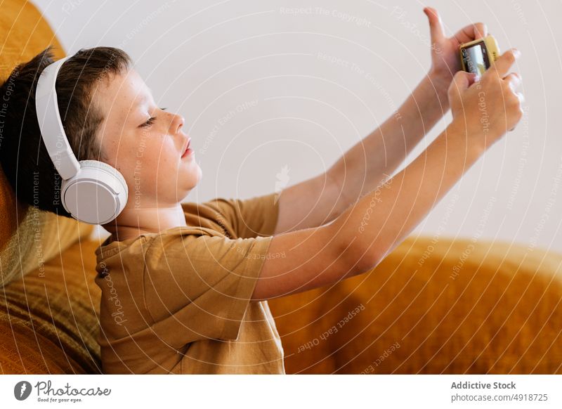 Boy sitting on a sofa with headphones and a mobile phone child boy home technology indoors kid young people serious concentrated cartoon movie lifestyle