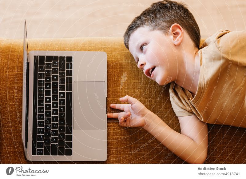Boy lying on a sofa using the laptop child computer boy caucasian technology male kid indoors home childhood little game internet play young digital at home