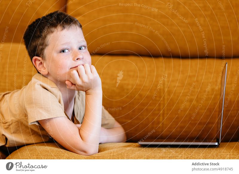 Boy lying on a sofa using the laptop child computer boy thoughtful caucasian technology male kid indoors home childhood little game pensive internet play young
