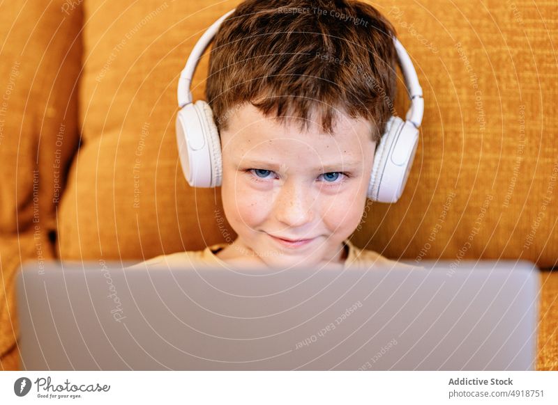 Boy sitting on a sofa with headphones on his head and using the laptop child smile computer happy boy caucasian technology male kid cartoon movie indoors home