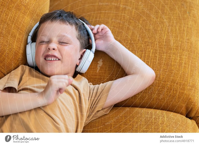 Happy boy lying on the sofa with eyes closed child kid headphones lying down playlist home bored music technology delight childhood little lifestyle leisure