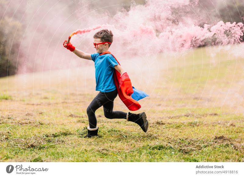 Little superhero with smoke bomb running around boy park excited costume play power lawn colorful bright smile child happy imagination fantasy adorable summer