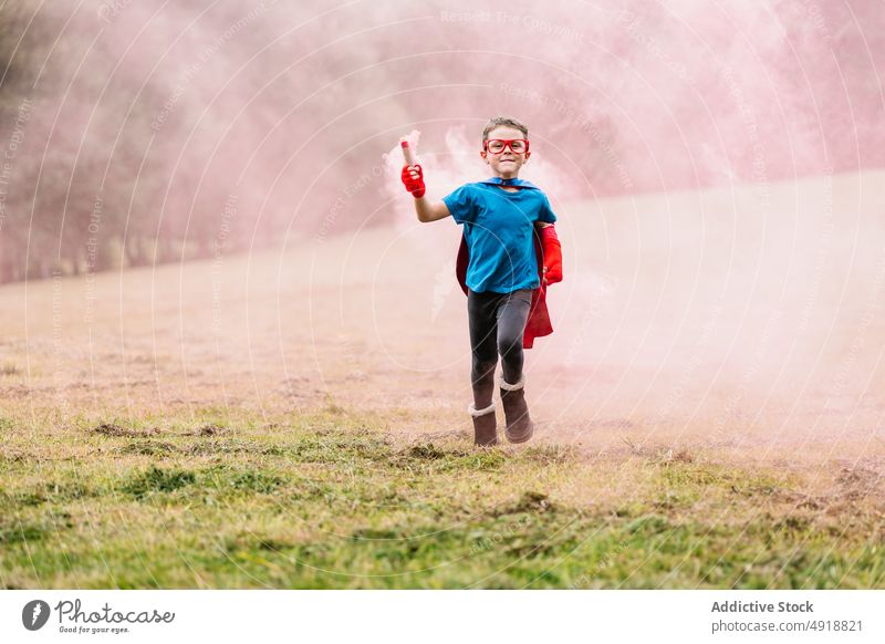 Little superhero with smoke bomb running around boy park excited costume play power lawn colorful bright smile child happy imagination fantasy adorable summer