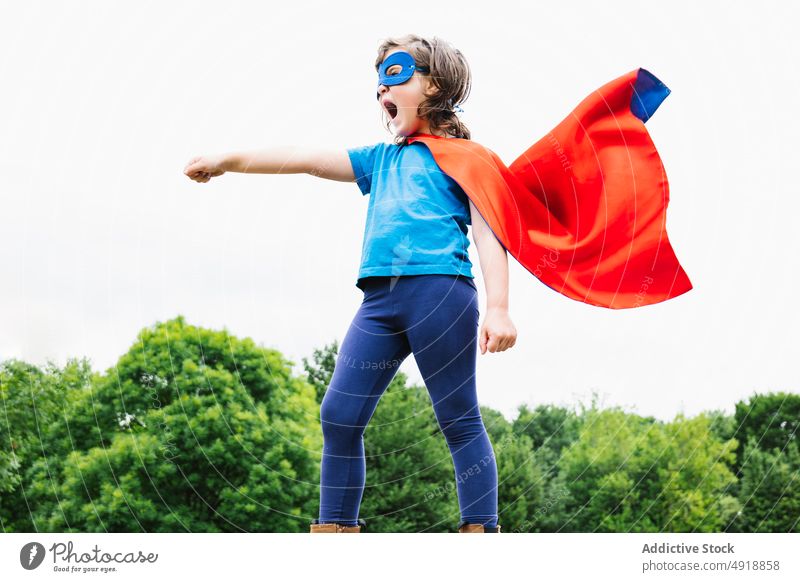 Excited girl in superhero costume in park scream play tree arm raised power cloudy female cape mask excited summer kid child daytime brave shout hand raised