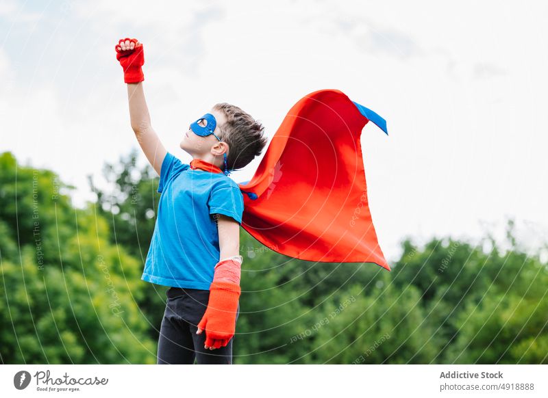 Excited boy in superhero costume in park scream play tree arm raised power cloudy cape mask excited summer kid child daytime brave shout hand raised activity