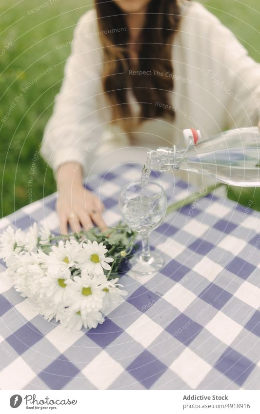 Unrecognizable woman pouring water in goblet in field glass table refreshment beverage countryside nature pastime recreation drink feminine summer female lady
