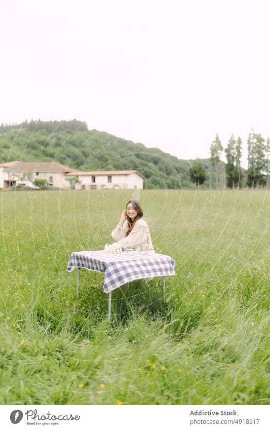 Positive woman sitting at table in field picnic countryside summer recreation nature grass pastime rest feminine smile beverage female dress optimist content