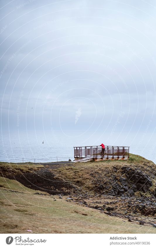 Traveler on viewpoint near sea traveler admire shore cloudy sky gray rest fence iceland outerwear weather cold tourist coast terrace journey wanderlust gloomy