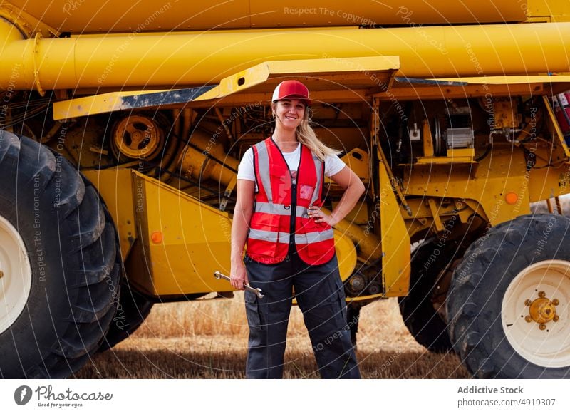 Positive woman with wrench near combine harvester worker instrument farmer agriculture countryside field tool supply mechanic technician positive satisfied