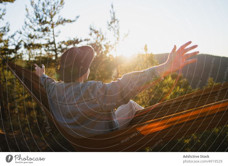 Faceless man resting in hammock in nature forest relax extended arms recreation woods leisure chill pastime headwear tree hat male summer plant sunshine journey