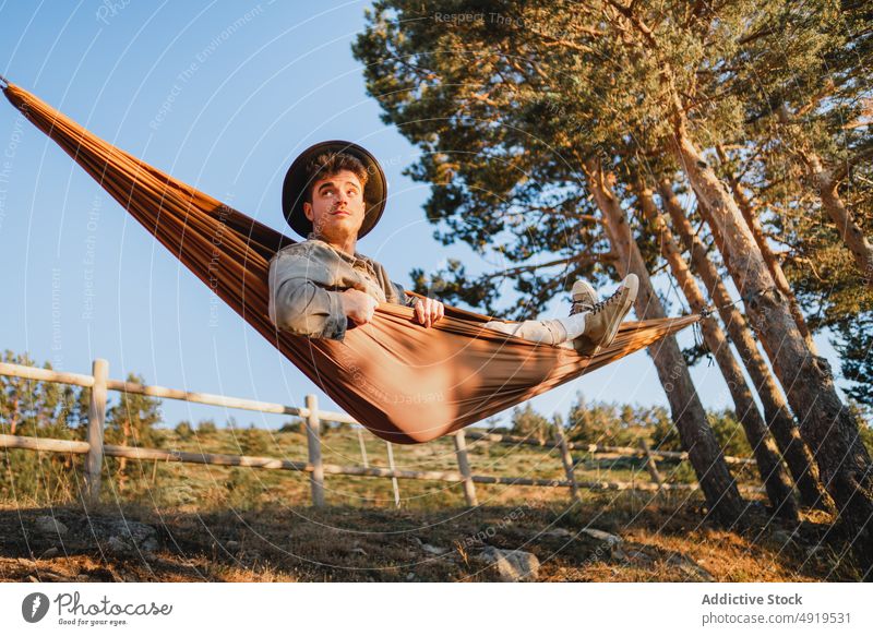 Man resting in hammock in nature man forest relax recreation woods leisure chill pastime headwear tree hat male summer plant sunshine journey summertime trendy
