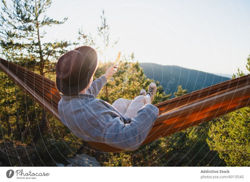 Faceless man resting in hammock in woods feather forest nature recreation leisure chill enjoy countryside trip adventure outstretch pastime headwear tree hat