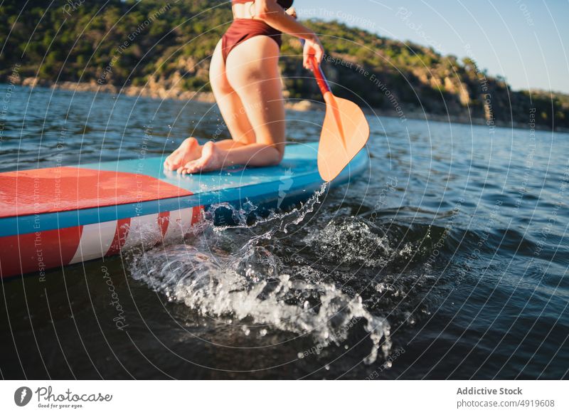 Woman floating on paddleboard in lake woman sporty surfer leisure hobby water row coast adventure sup board shore nature equipment rest rock wellbeing summer