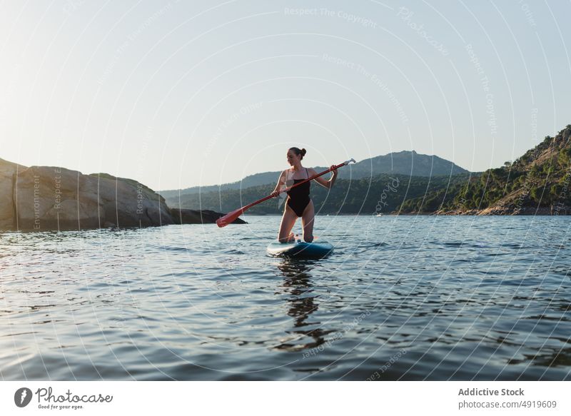 Woman floating on paddleboard in lake woman sporty surfer leisure hobby water row coast adventure sup board shore nature equipment rest rock wellbeing summer