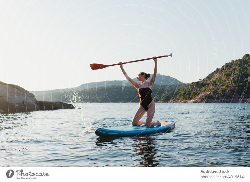 Woman in swimwear floating on paddleboard woman sporty surfer hobby lake water row practice tree coast equipment sup board adventure leisure shore nature