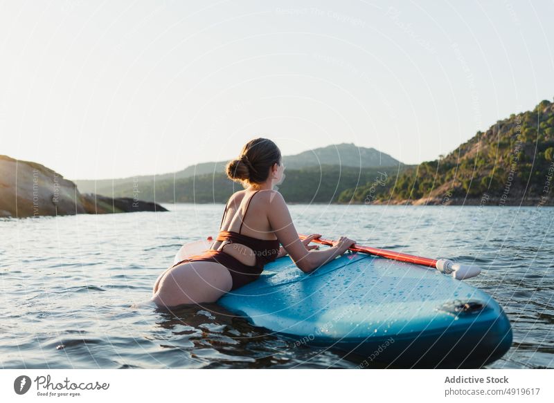 Woman lying on paddleboard in lake woman leisure hobby water rest nature wellbeing swimwear summer sup board slender shore float relax forest vacation coast