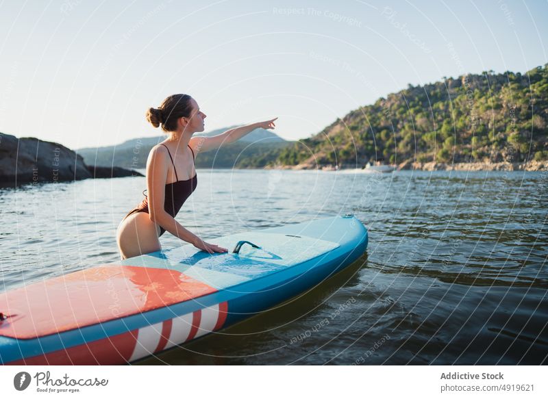 Woman standing in lake with surfboard woman surfer leisure hobby pointing water nature wellbeing trip summer seaside sup board paddleboard shore coast woods